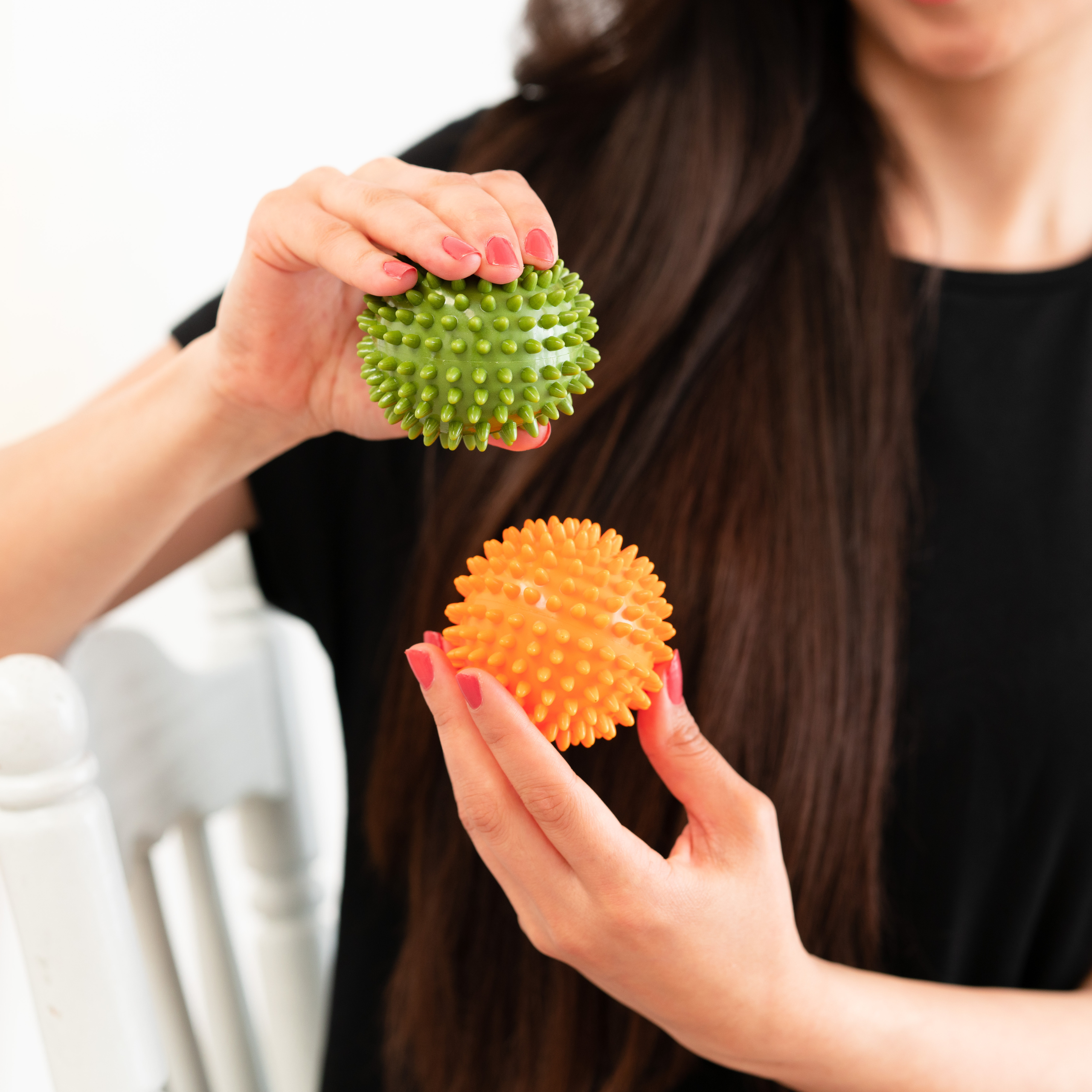 Frau hält zwei Igelbälle, einen grünen Ball ist weich und einen orangefarbenen, für Handmassage ist hart.